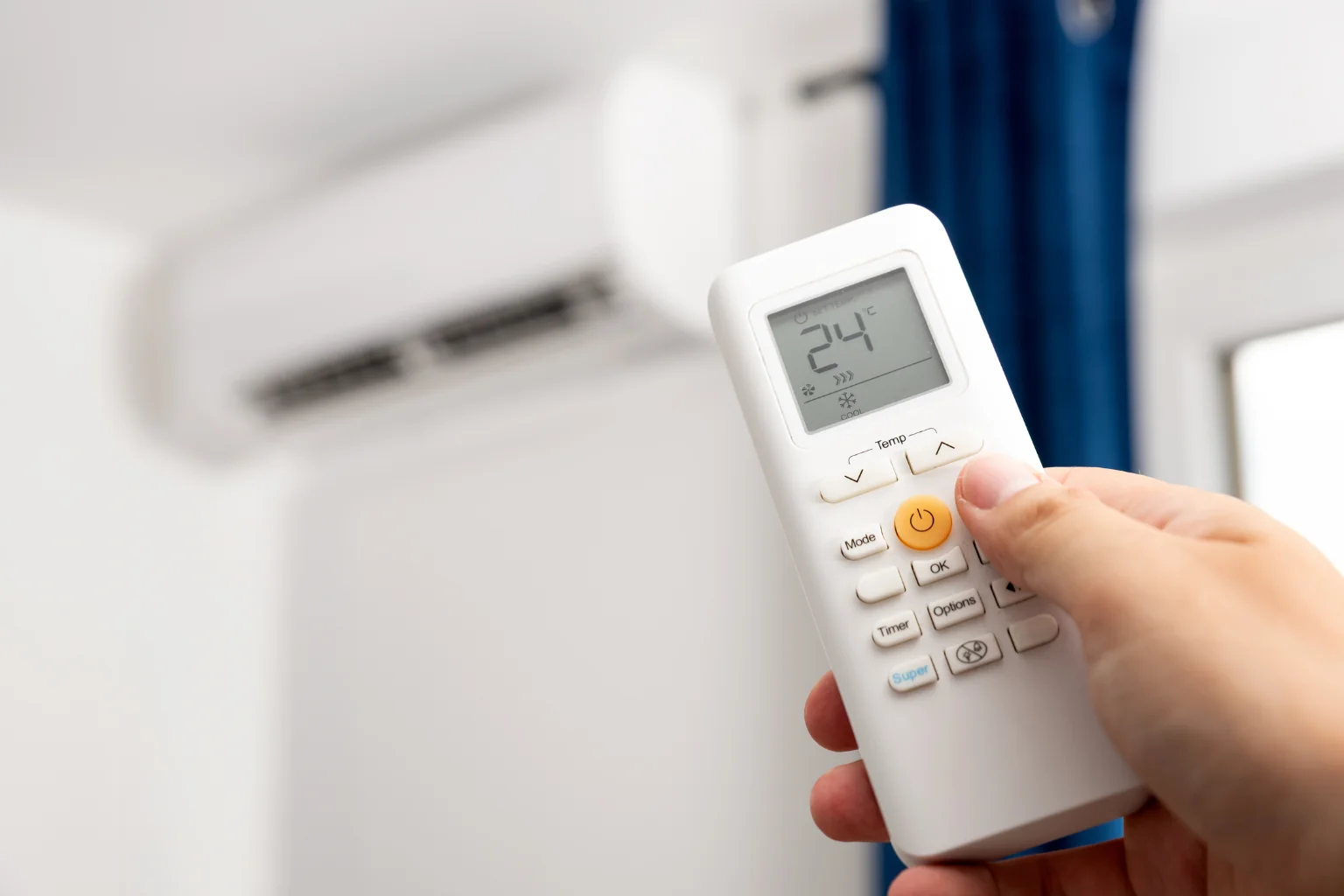 Рука тримає пульт кондиціонера з температурою 24°C на дисплеї